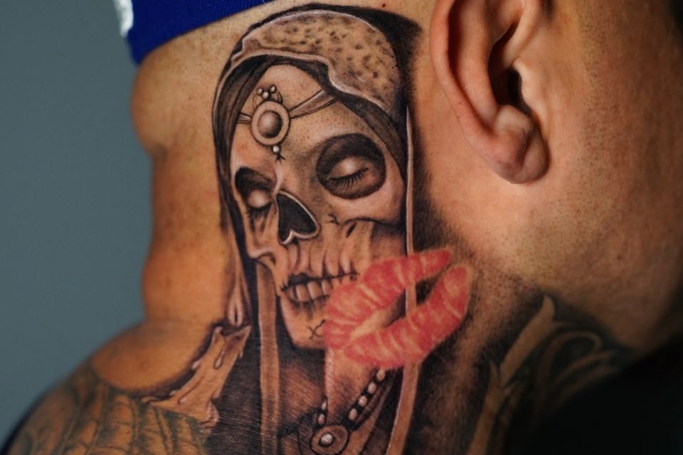 Image of a man in a ball cap with a neck tattoo of a princess skull in black, white and grey with a superimposed set of red lips
