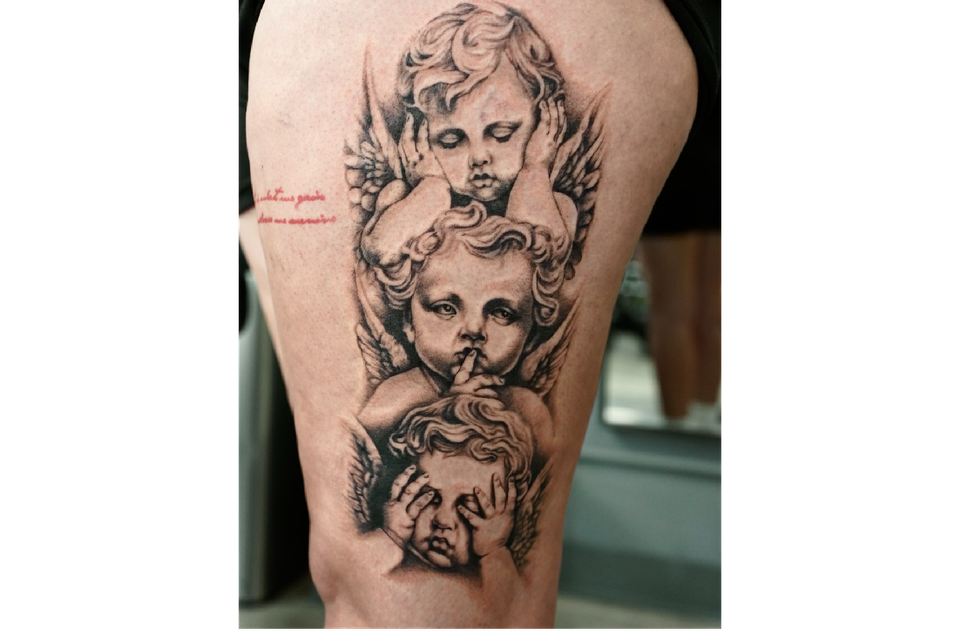 Image of a womans outer left thigh with a tattoo of 3 cherubs set vertically in black ink