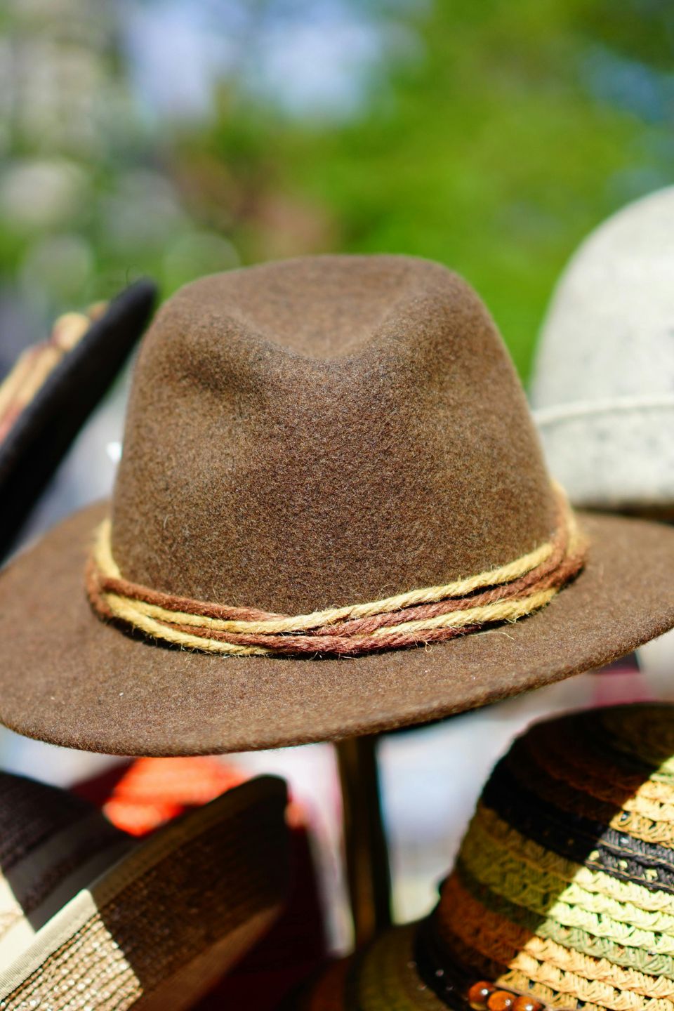 black, brown, white, and twead hats in a stand in the outdoors. 