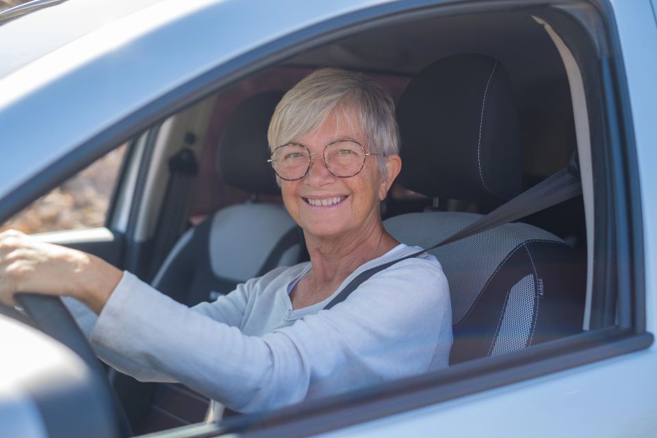 Senior woman sitting in her newly bought car looking out the window smiling joyfully
