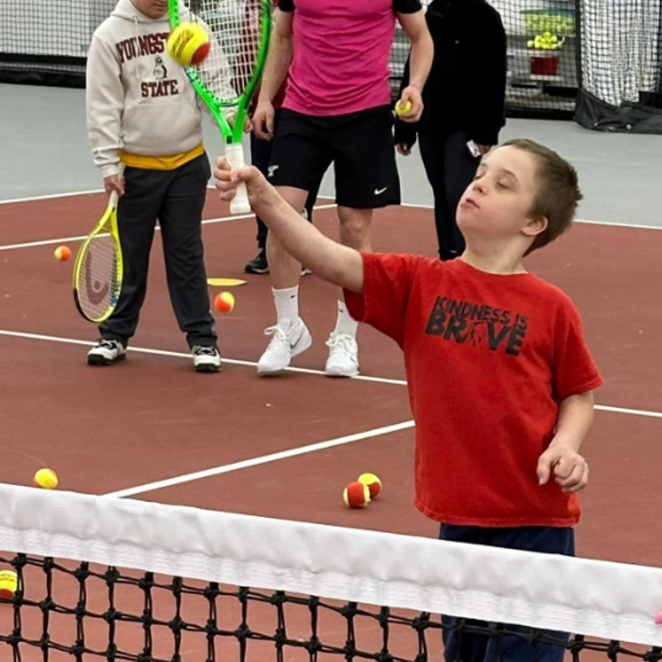 Participant with Down syndrome practicing tennis skills with instructors during a Down Syndrome Association of the Valley adaptive sports program.