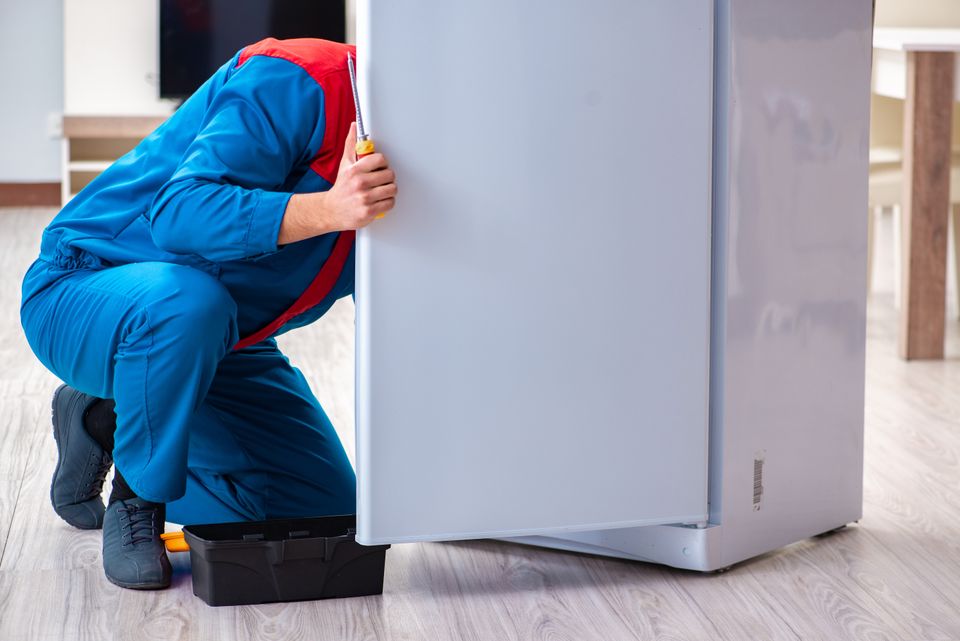 A repair man fixing a broken refrigerator 