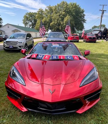 Red sports car decorated with American flags and patriotic decorations for a Fourth of July parade.