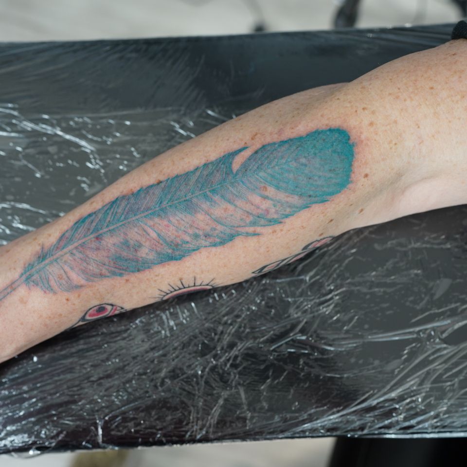Image of a large blue feather tattoo on the forearm of a man