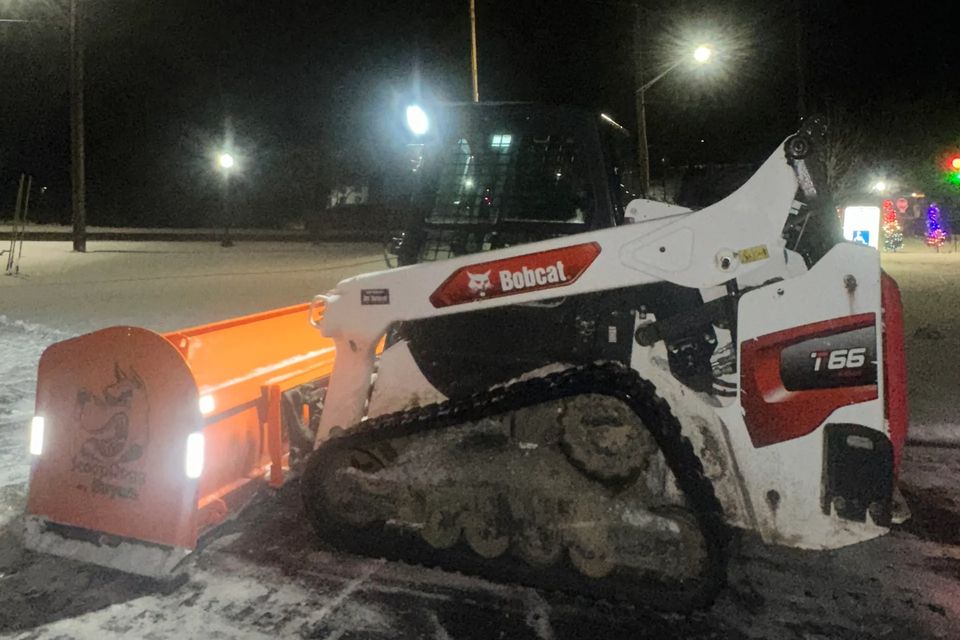 A snow plow clearing snow from a parking lot at night as part of R.E.P. Companies' snow removal services.