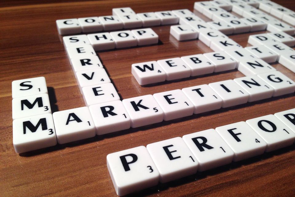 table with scrabble tiles arranged in a way so the word marketing is in the center of the table. The words server, shop, website, tracking, performance and more web presence related words can be read as well.