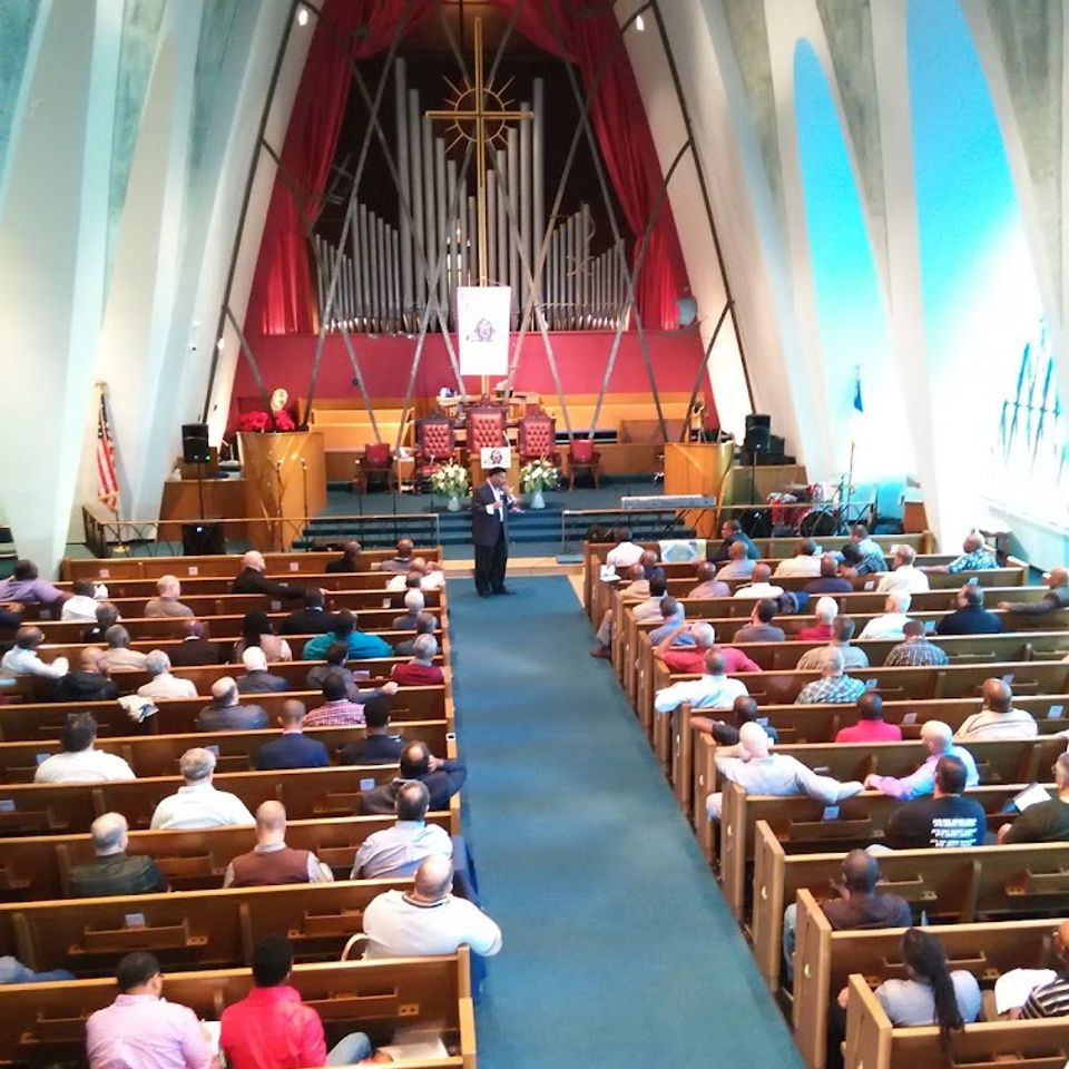 Congregation gathered for worship inside Grace Evangelistic Temple Church, with attendees seated in pews facing the sanctuary and pipe organ.