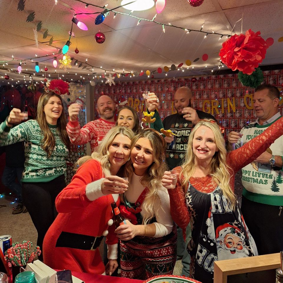 Group of guests in Christmas attire raising drinks and smiling at a holiday gathering