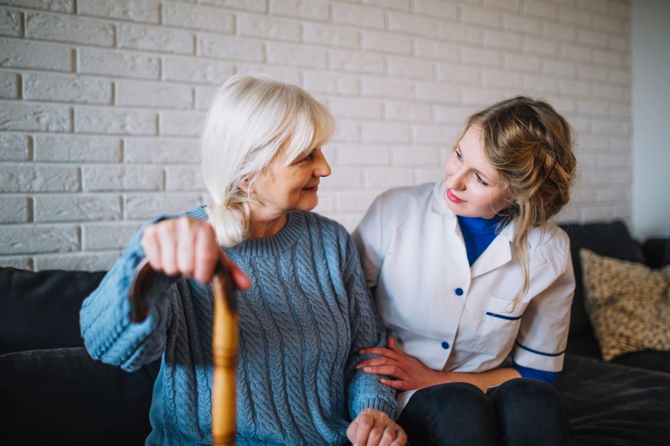 A nurse sitting down with a female patient who has a cane