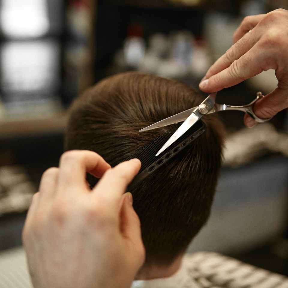 Close-up of a barber cutting a client's hair with scissors and a comb in a barbershop.