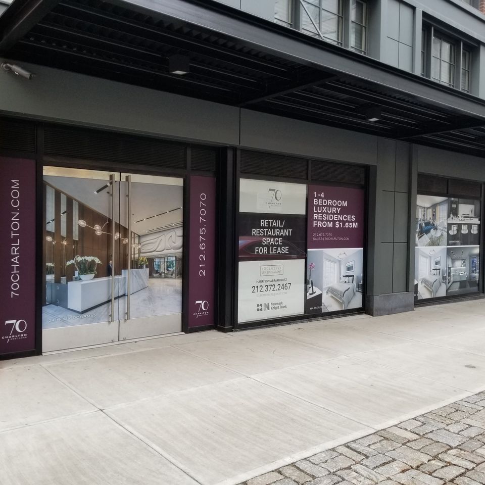 Deep red and white printed vinyl panels on storefront windows and columns beneath a building canopy