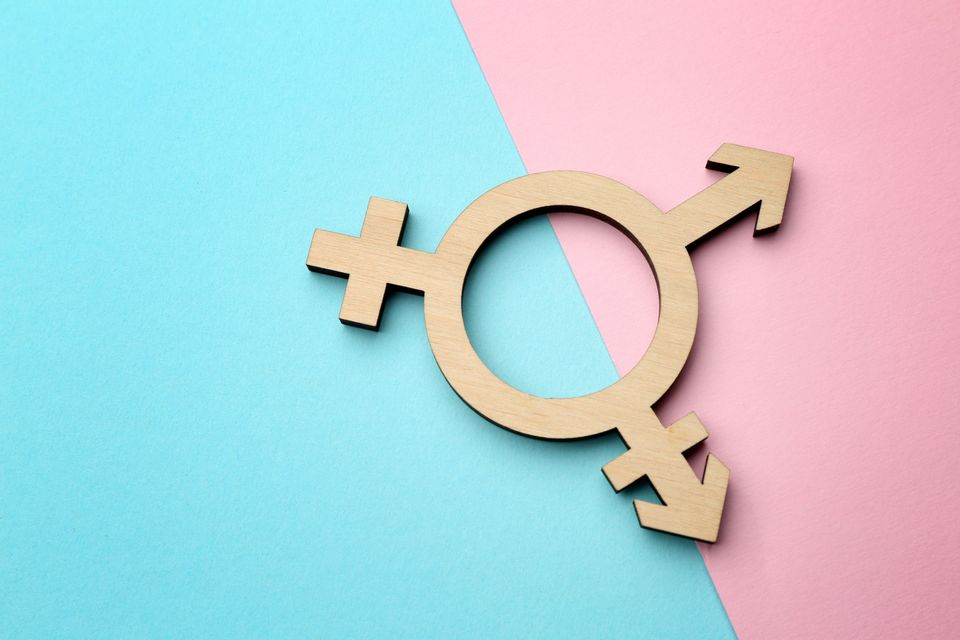 Overlapping metallic gender symbols on a pink and blue background  representing transgender  nonbinary  and gender diverse identities.