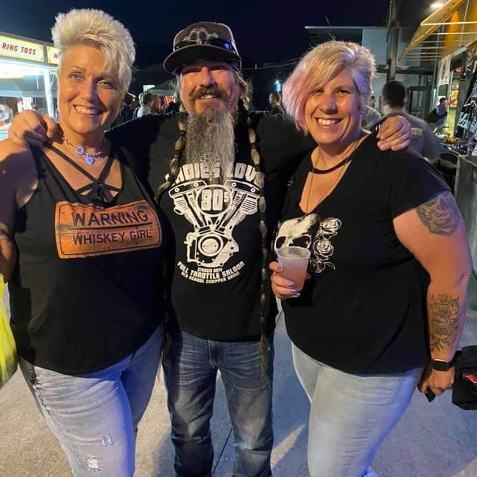 Two women and a man posing together at an outdoor nighttime event.