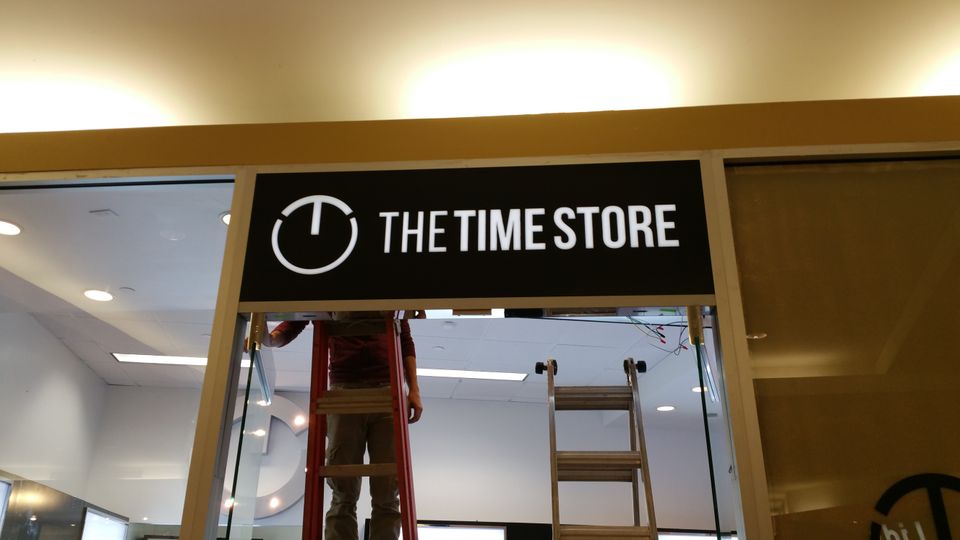 Installer on a ladder mounting an illuminated stencil cut sign above a storefront entrance