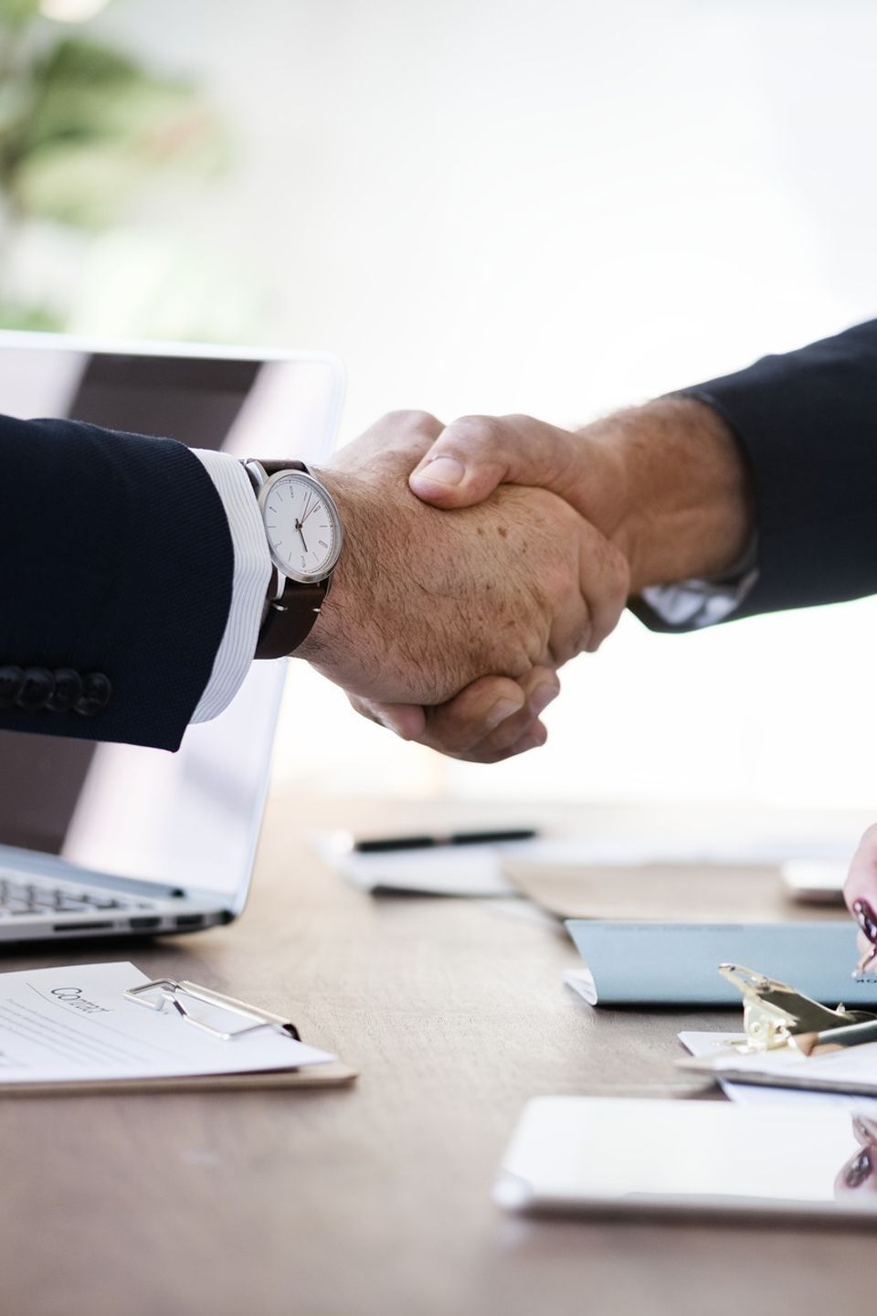 Two business owners shaking hands over a desk and some papers
