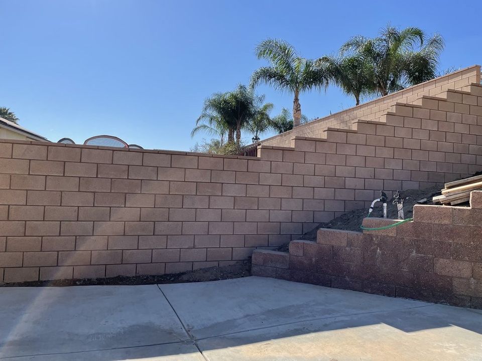 Custom block wall and retaining wall construction in backyard with concrete patio and privacy wall