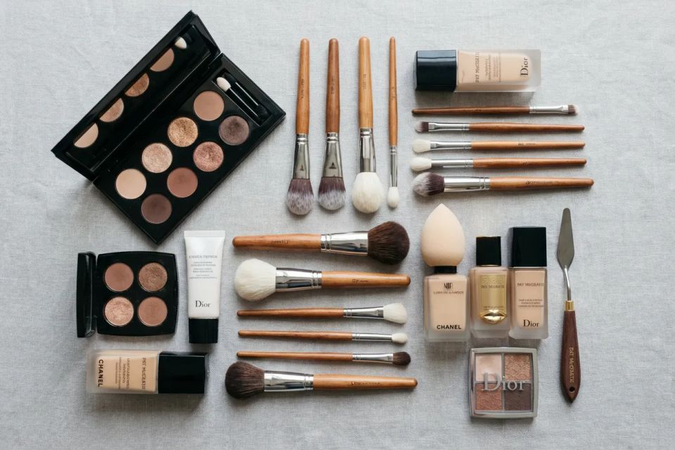 Professional makeup artist kit flat lay featuring luxury foundation, eyeshadow palettes, and clean brushes on a neutral background
