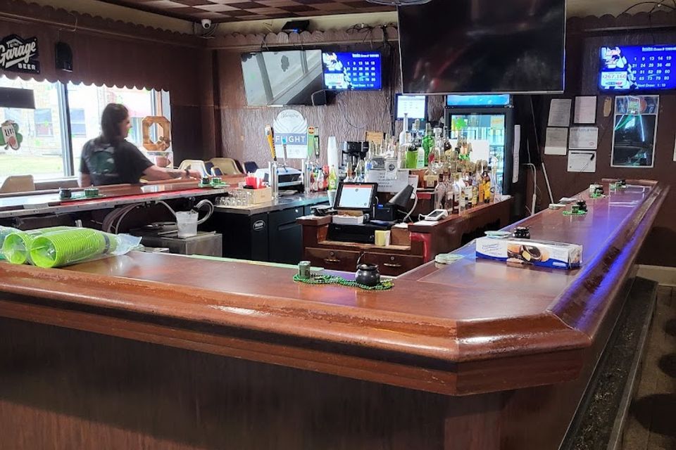 Interior of Village Tavern bar with wooden counter, drinks, and TVs