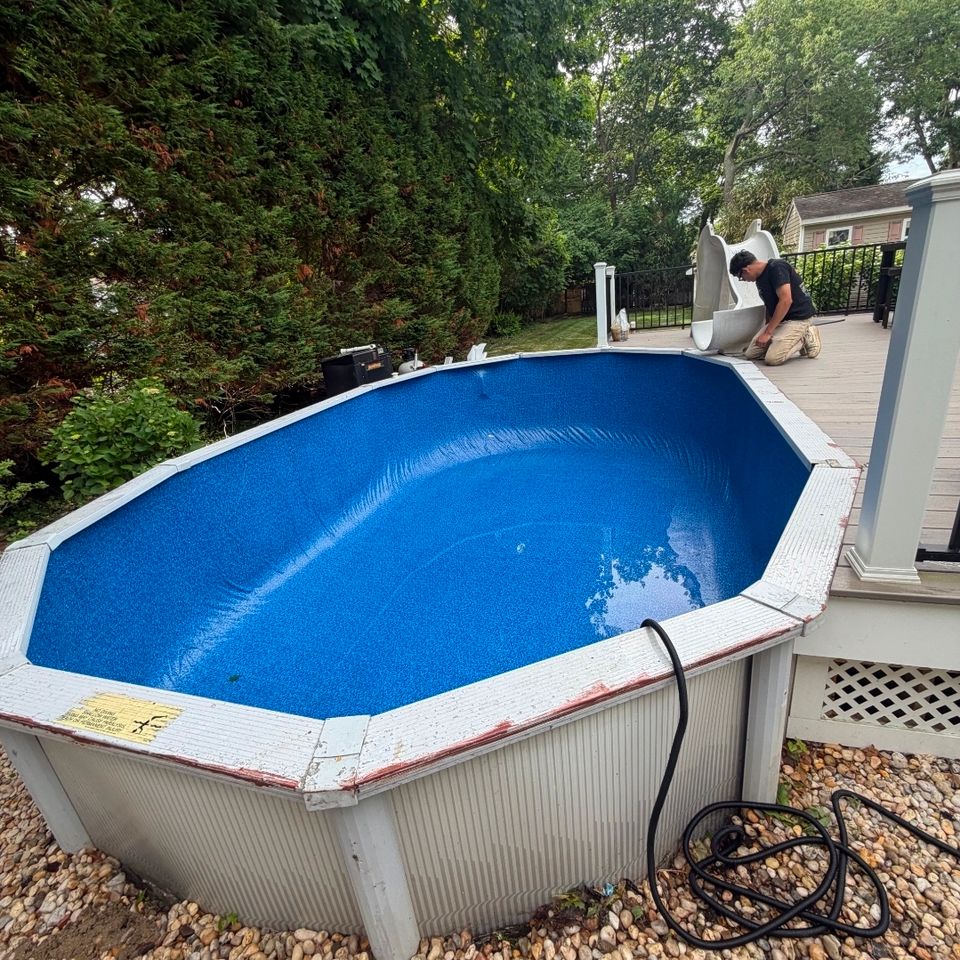 Technician working on an oval above ground pool with a new blue liner beside a backyard deck