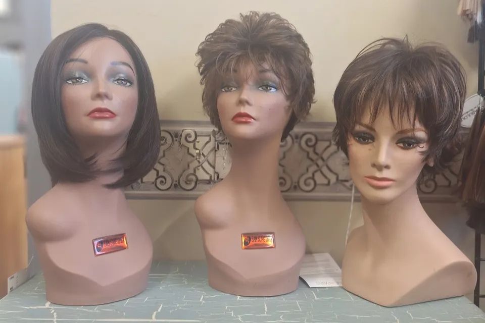 Three mannequin heads displaying different wig styles, including a sleek bob, a short layered cut, and a textured pixie-style wig inside Shears Wigs & Hairpieces Salon.