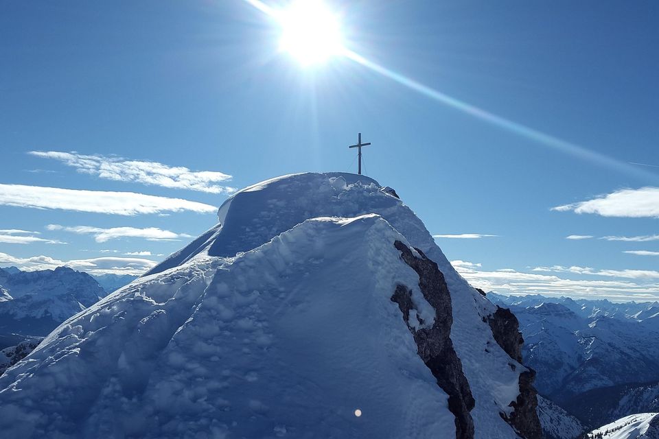 A cross on top of a snow-covered mountain with the sun shining bright