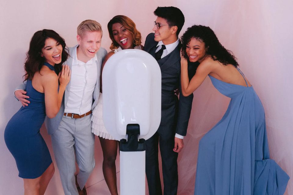 Group of friends dressed up and posing together in front of a digital photo booth with a pink backdrop