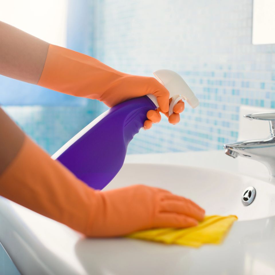 Gloved cleaner spraying and wiping bathroom sink during house cleaning service in Virginia Beach VA