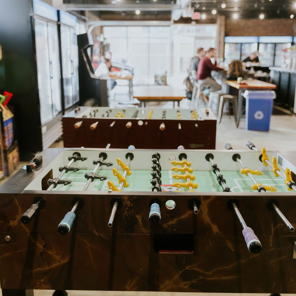 Foosball table with arcade machines and bar in background