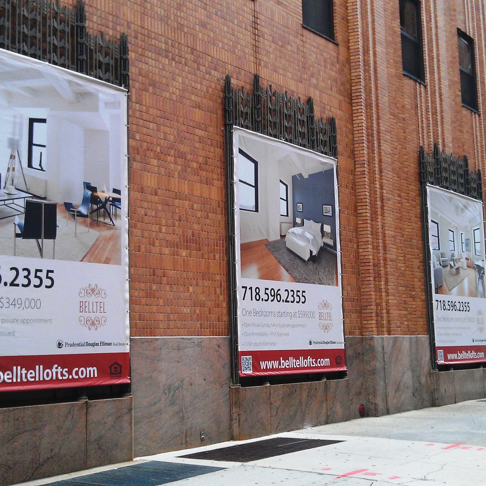 Row of printed vinyl banners advertising Belltel Lofts on a brick building facade in Brooklyn