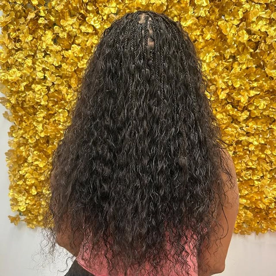 Long boho knotless braids with curly ends styled against a gold floral wall in Los Angeles CA