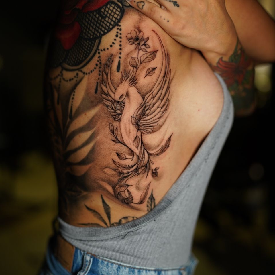 Image of a large tattoo on the side and back of a woman of a Phoenix and plant leaves