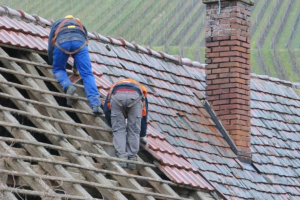 Two person putting roof tiles on roof at daytime