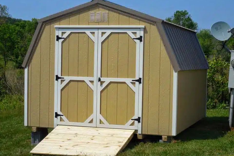 Tan mini barn shed with white trim doors and wood ramp installed in East Tennessee