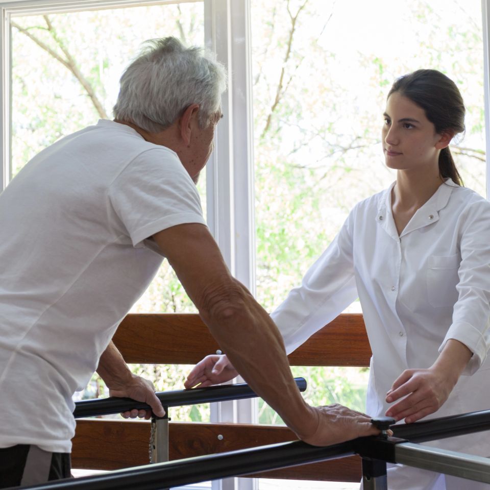 Senior man with his physiotherapist doing a physical rehabilitation in a parallel bars