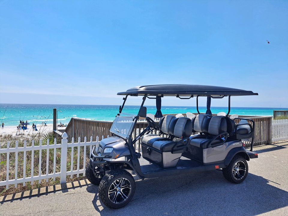 Gray six-passenger golf cart rental parked at a beach access boardwalk overlooking turquoise water in Destin Florida