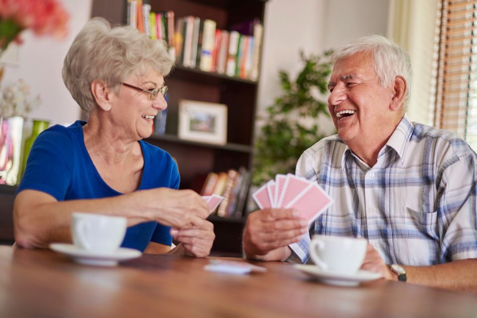 Senior couple laughing over card game and coffee during companion care on Long Island NY