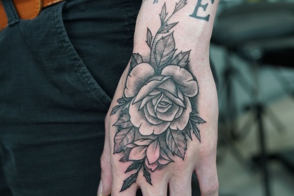 Image of a rose tattoo on a mans hand in black and grey