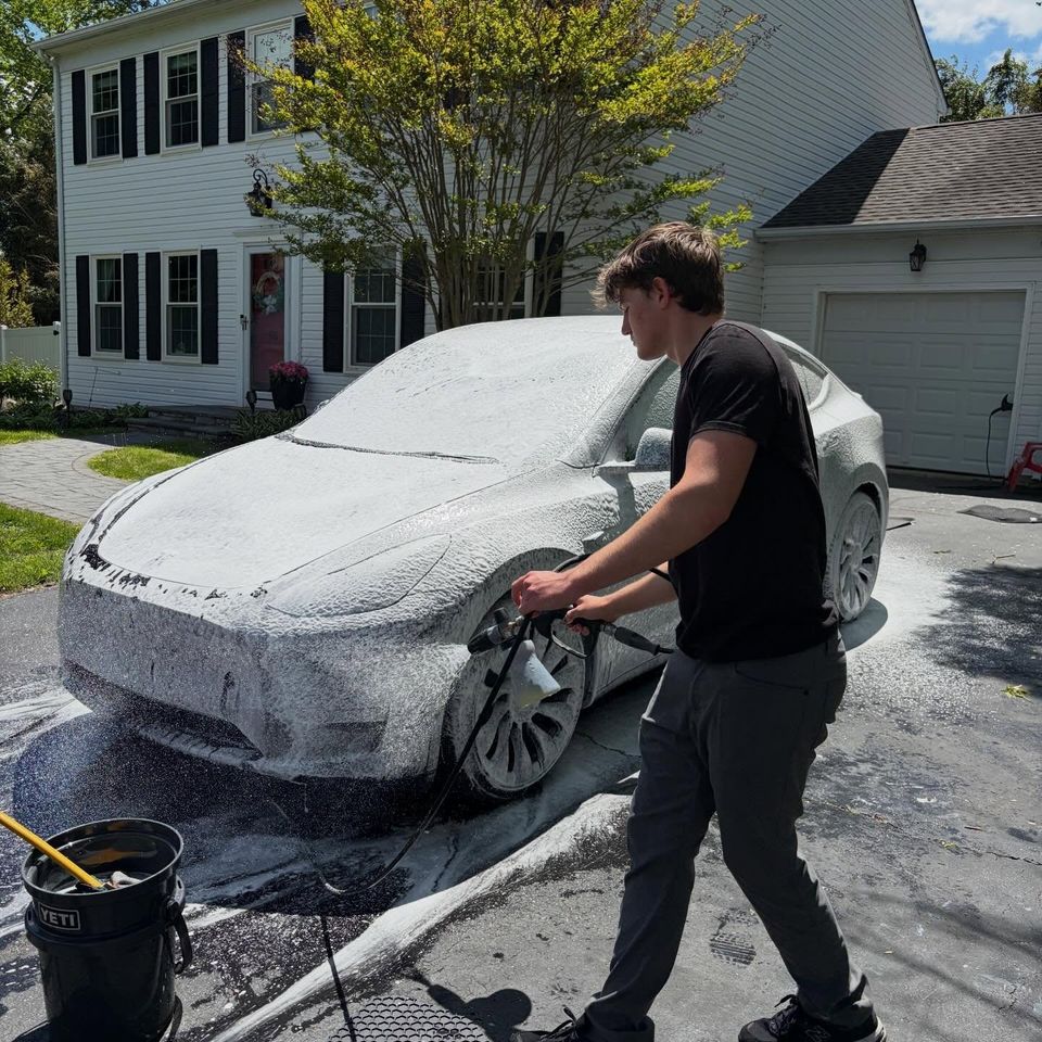 Detailer spraying thick snow foam onto a Tesla Model Y with a foam cannon during a mobile wash in Wilmington DE