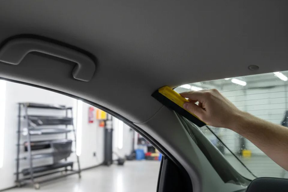 Professional window tint installer applying film to rear windshield for a bubble-free finish.
