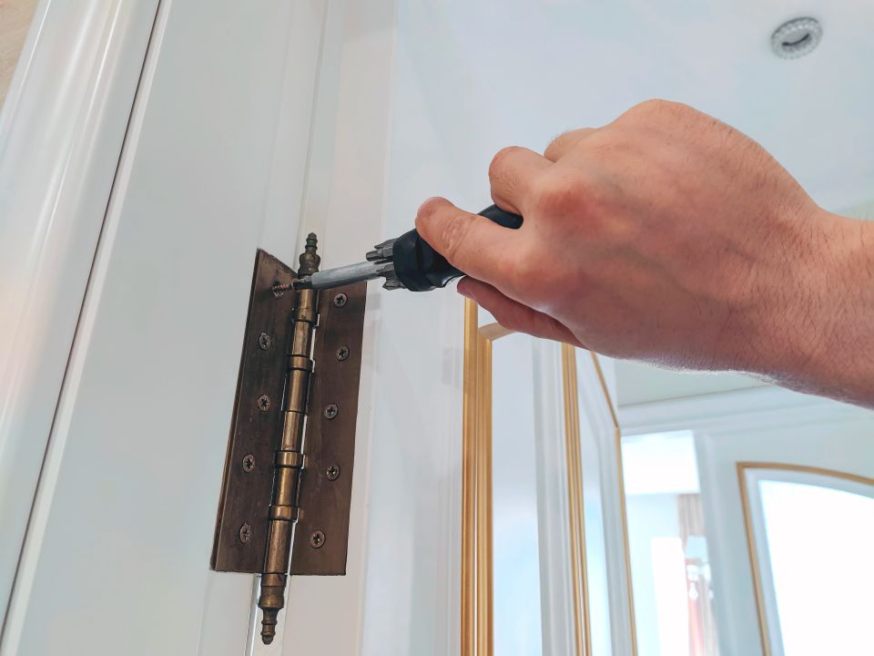 A person screwing a door hinge in during a door installation job