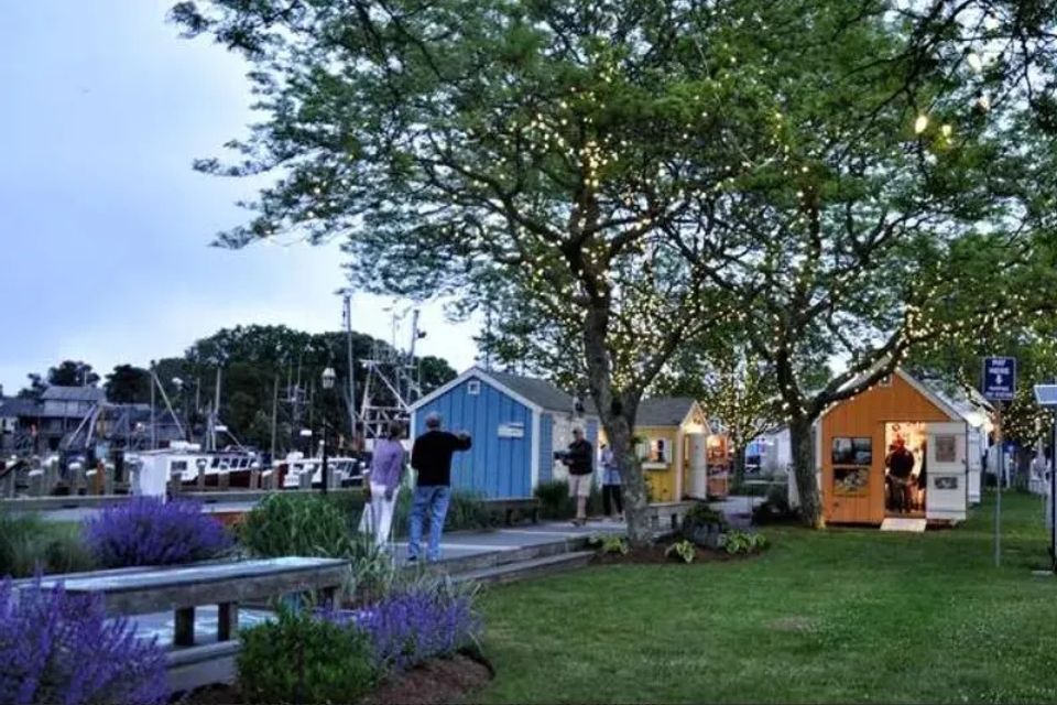 Purple flowers and green grass and trees, at the Artist Shanties that are very colorful