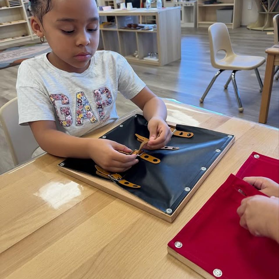 Preschool girl practicing a buttoning dressing frame during Montessori practical life work in Palmdale CA