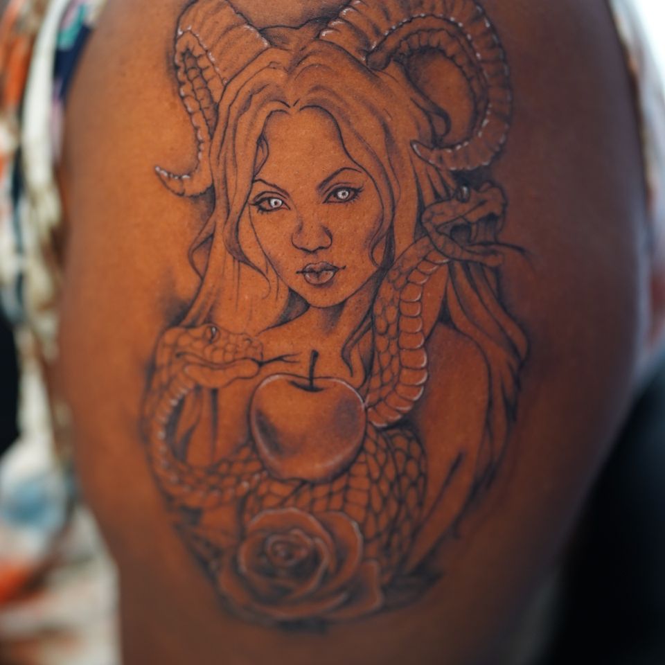 Image of a large shoulder tattoo of a woman with horns and a serpent and an apple with white highlights
