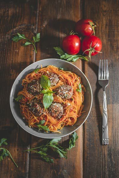 Spaghetti and meatballs on a wood table with fresh tomatoes and basil strewn about 