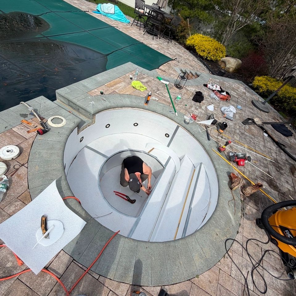 Technician rebuilding a round spa with new panels next to a covered inground pool