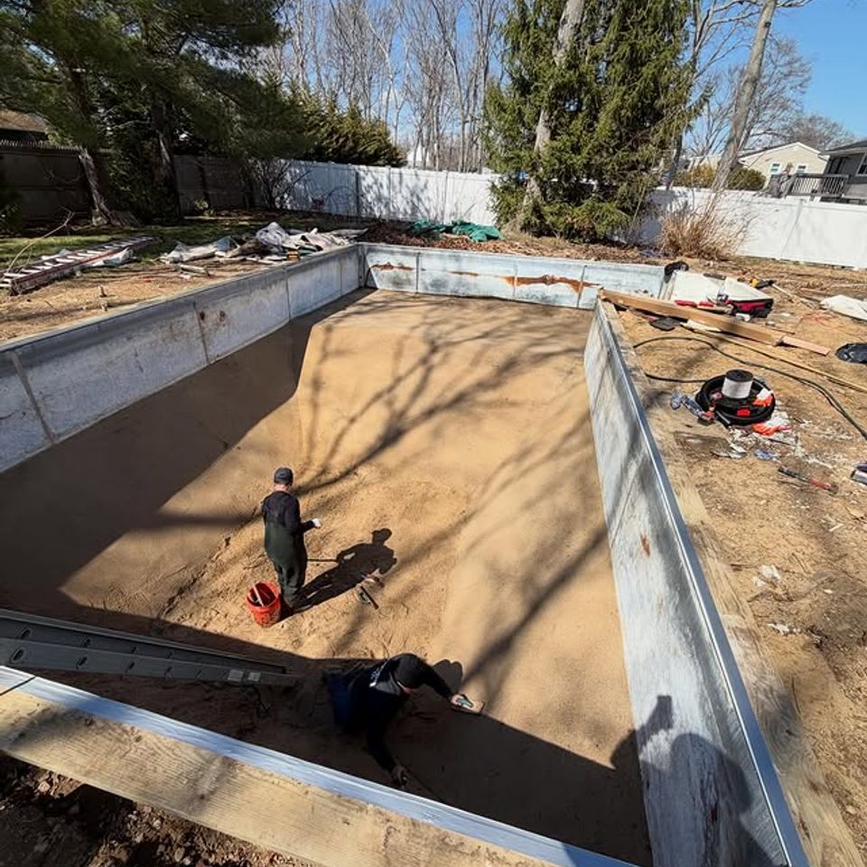 Crew smoothing the sand base inside a steel pool wall during an inground pool install on Long Island