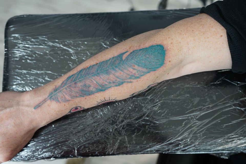 Image of a large blue feather tattoo on the forearm of a man