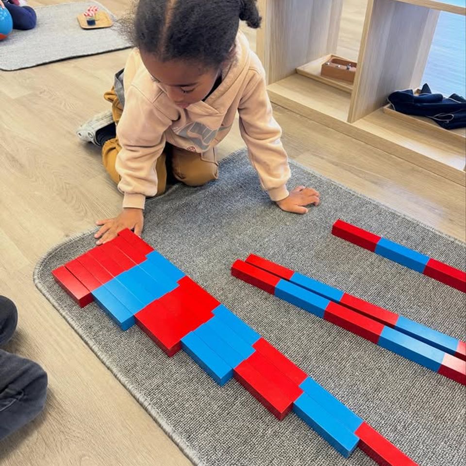 Child arranging red and blue Montessori number rods on a classroom rug during math work in Palmdale CA