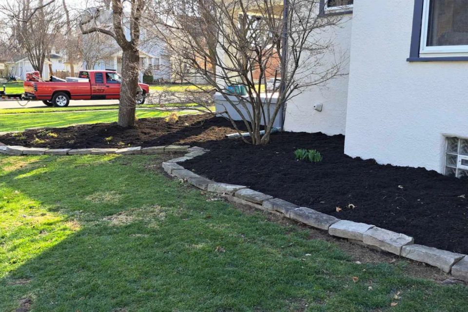 Front yard landscape with fresh black mulch, stone edging, and planting beds surrounding the home.