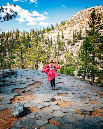 A person in hot pink on top of the Devil's postpile showing off the hexagonal shapes that were made by molten lava and cooling 